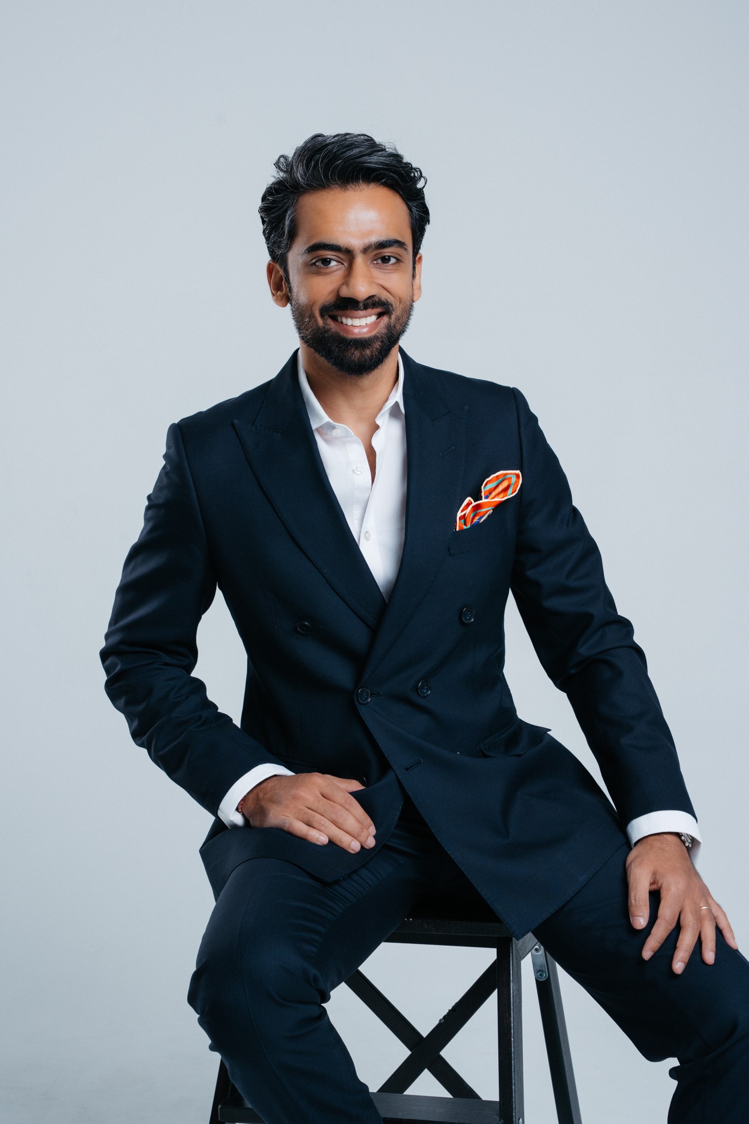 Kartik seated in his navy double-breasted suit